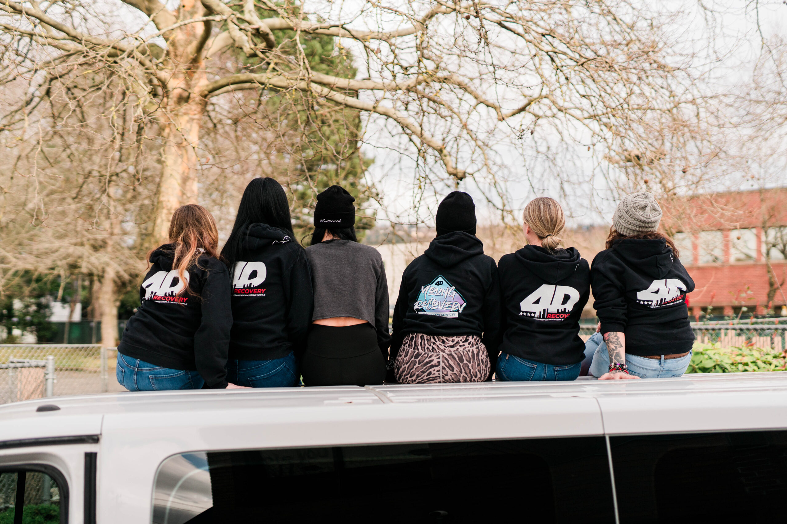 Six women sitting on top of a van, all wearing 4D sweatshirts